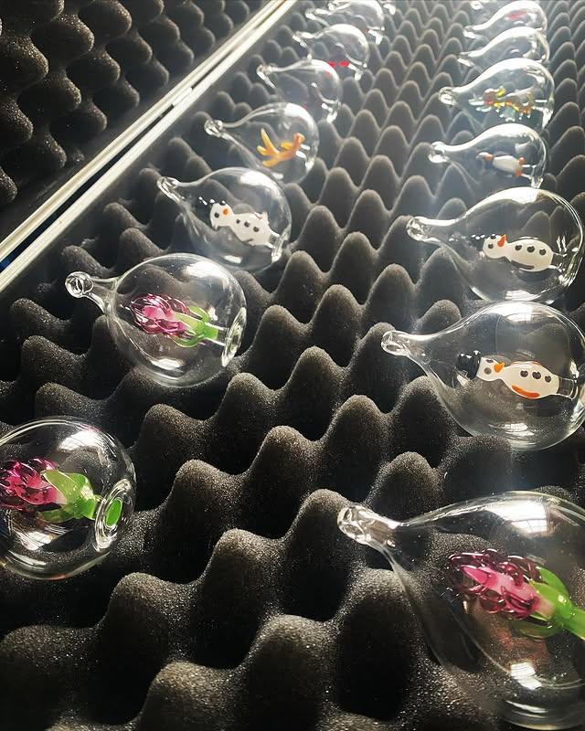 Clear glass ornaments with enclosed flowers, birds, and small figures nested in black foam